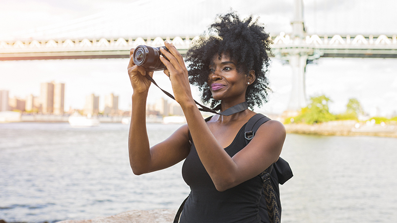 A woman taking a photo with a camera along a waterfront in a city