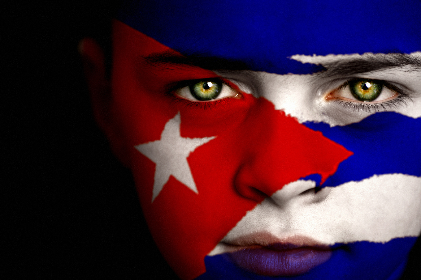 Portrait of a boy with the flag of cuba painted on his face.