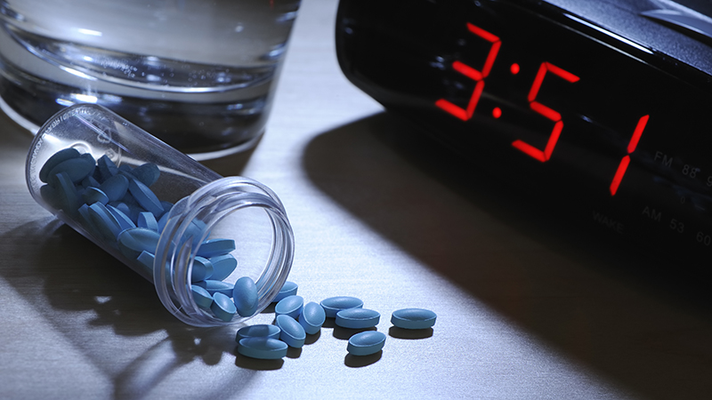An up-close view of an alarm clock, pills and glass of water