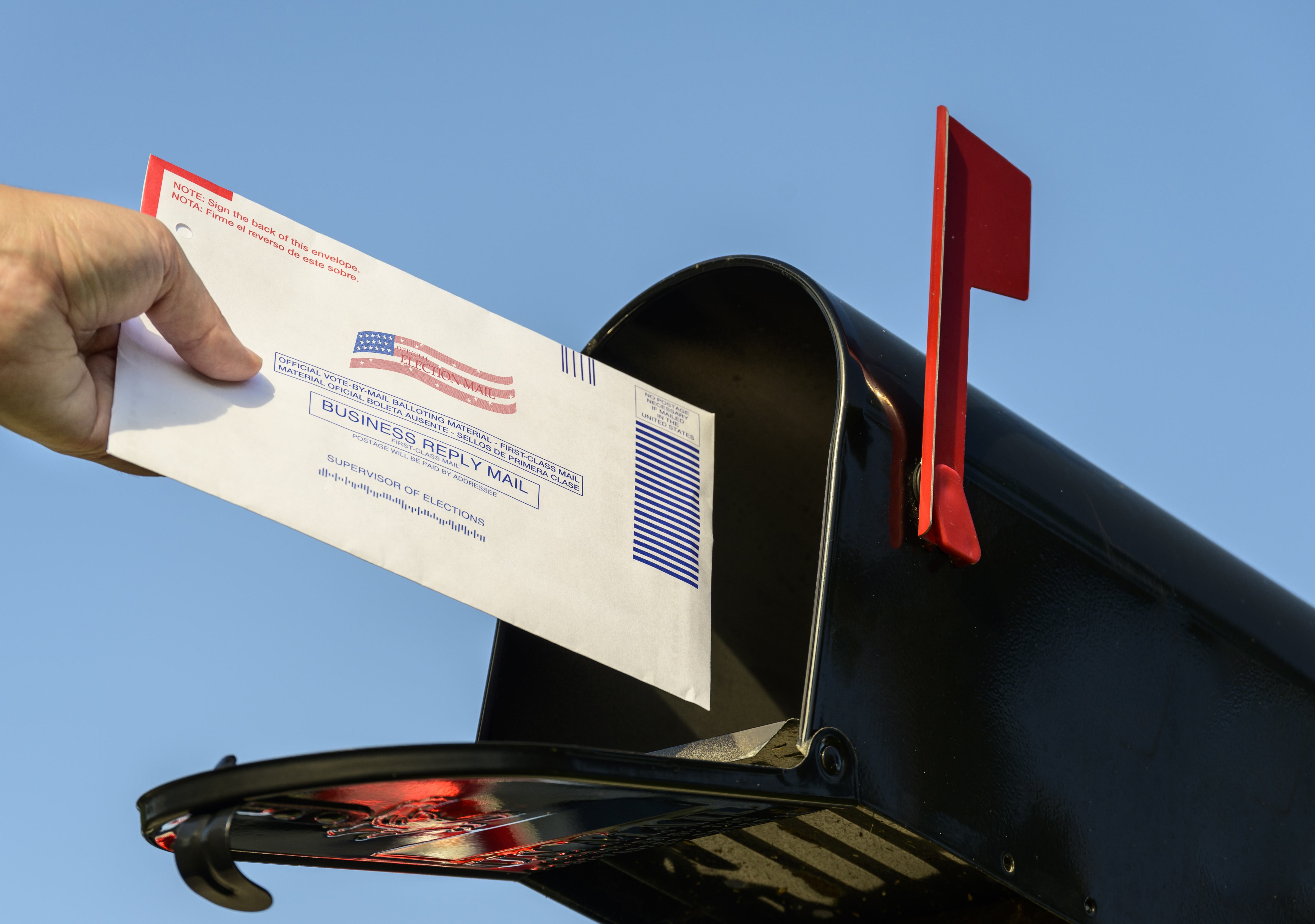 Woman's hand placing a 2020 mail-in election ballot in a rural mailbox