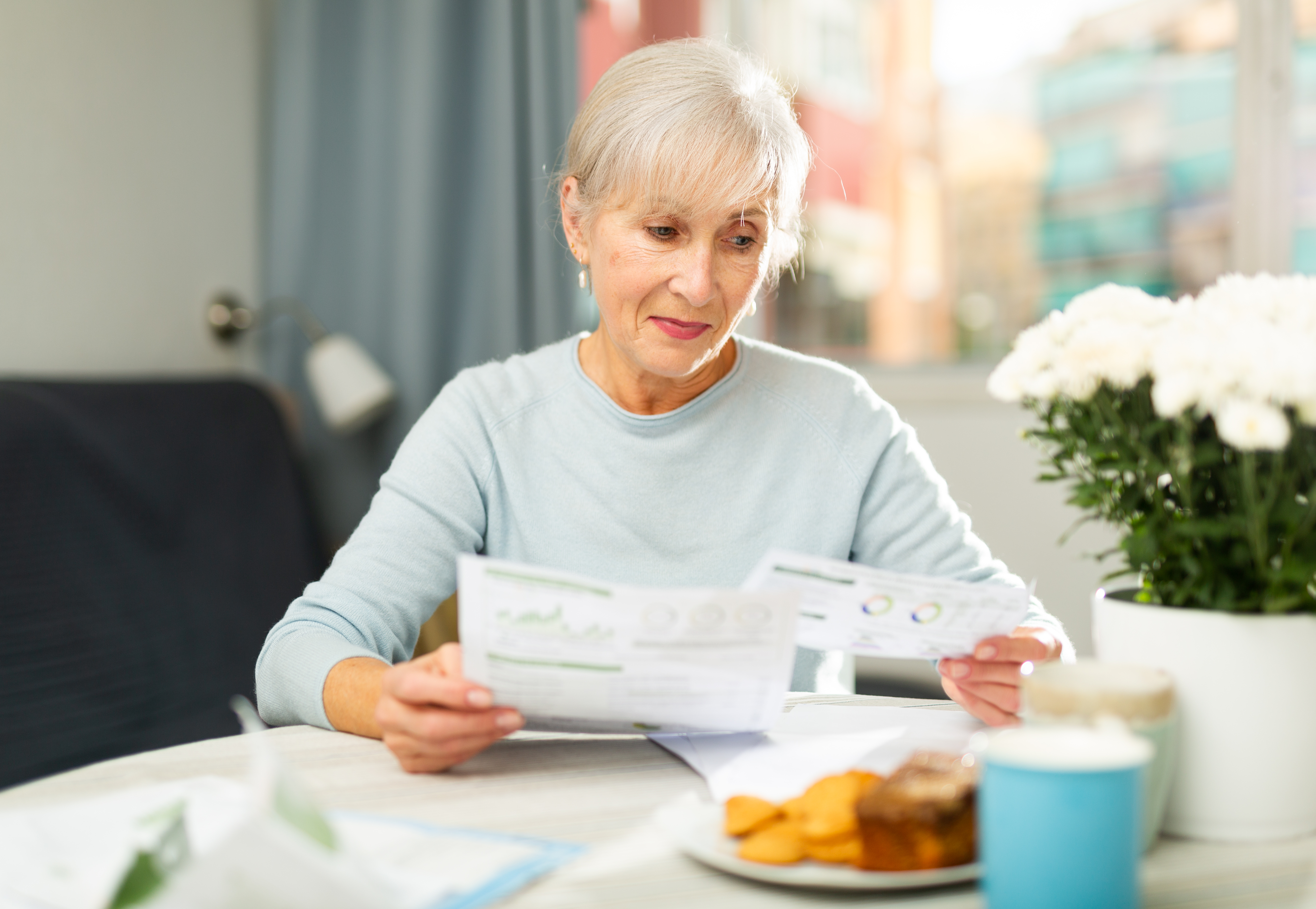 Senior woman reading papers with interest at home table