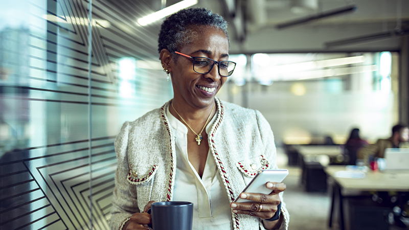 A woman looking at her smartphone while holding a coffee mug in her other hand