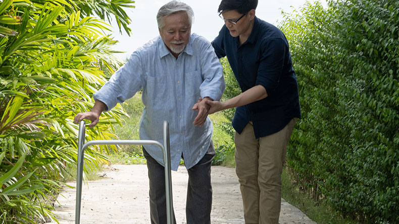 Man helps older man walk with walker