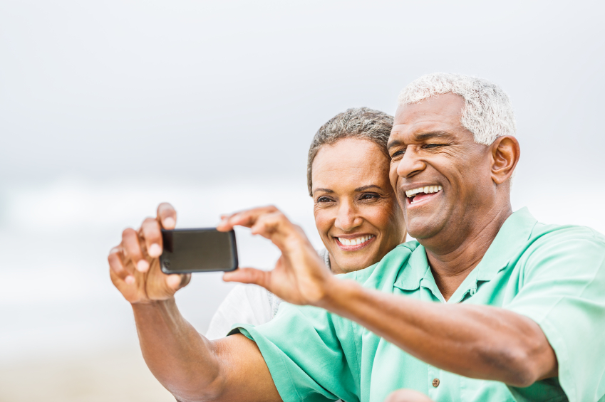 Senior African American couple having fun with smartphone on bea