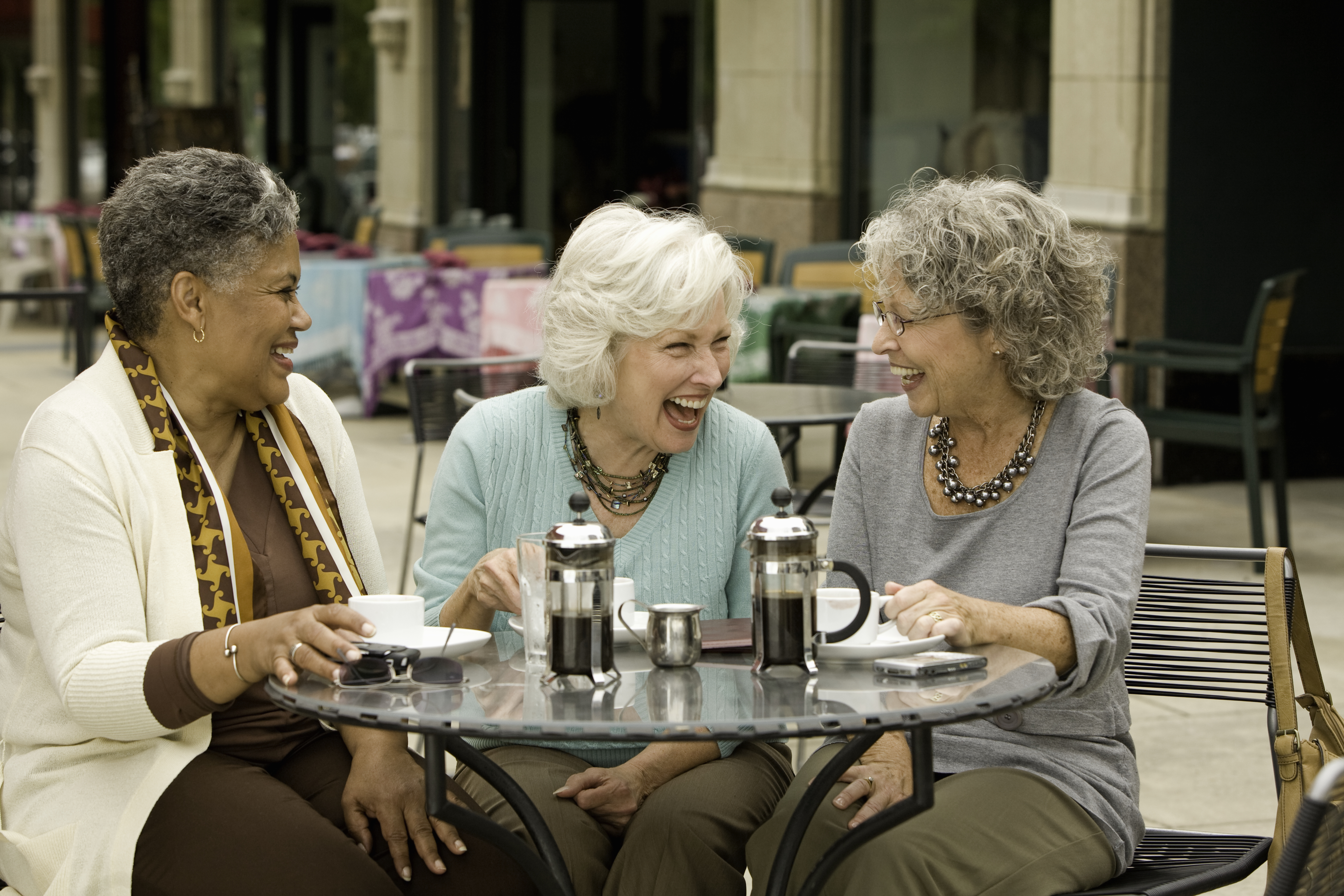 Three senior women sitting at cafe table, laughing