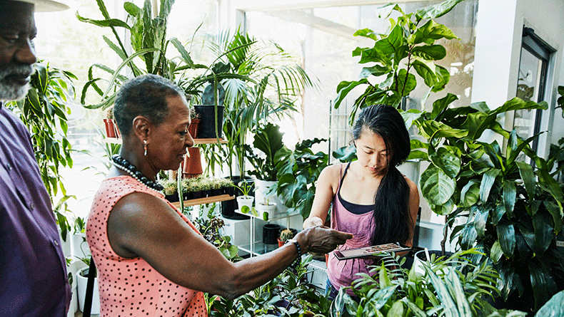 Senior woman handing credit card to shop owner processing payment on digital tablet