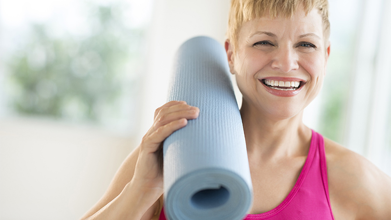 A woman holding a yoga mat on her shoulder