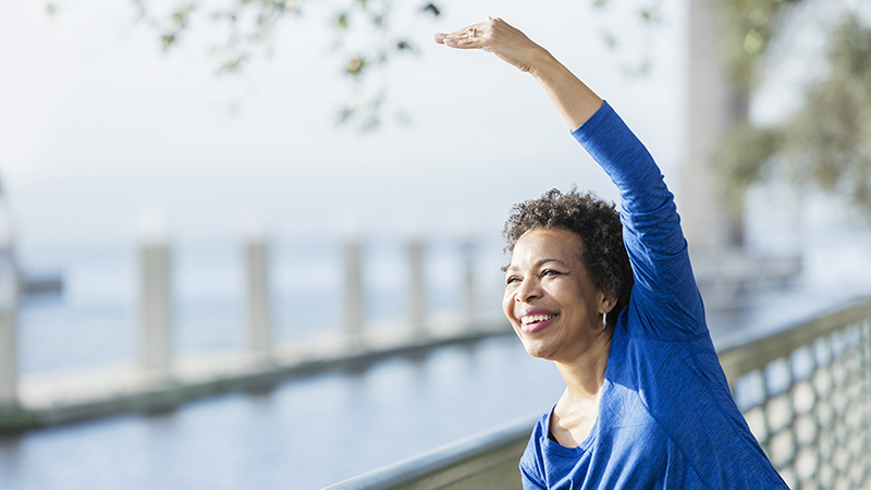 A woman stretching her arm over her head along a waterfront