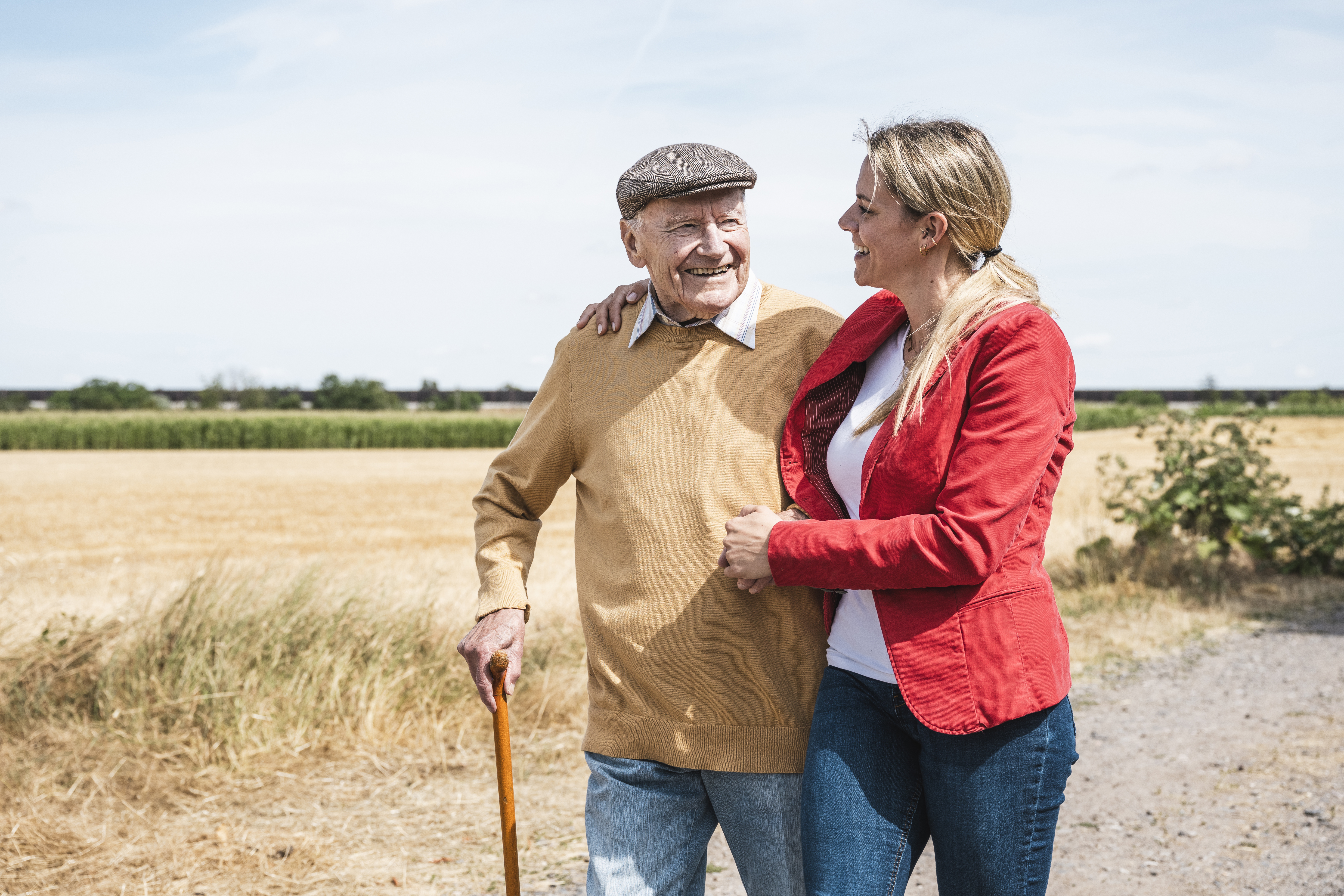 Smiling senior man walking with woman by field on sunny day