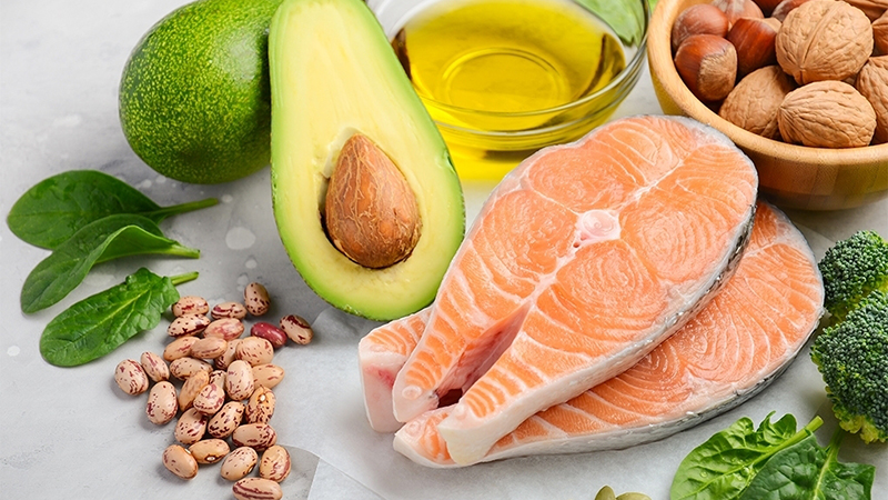 A close-up view of salmon, beans, avocado, olive oil, spinach, broccoli and mixed nuts