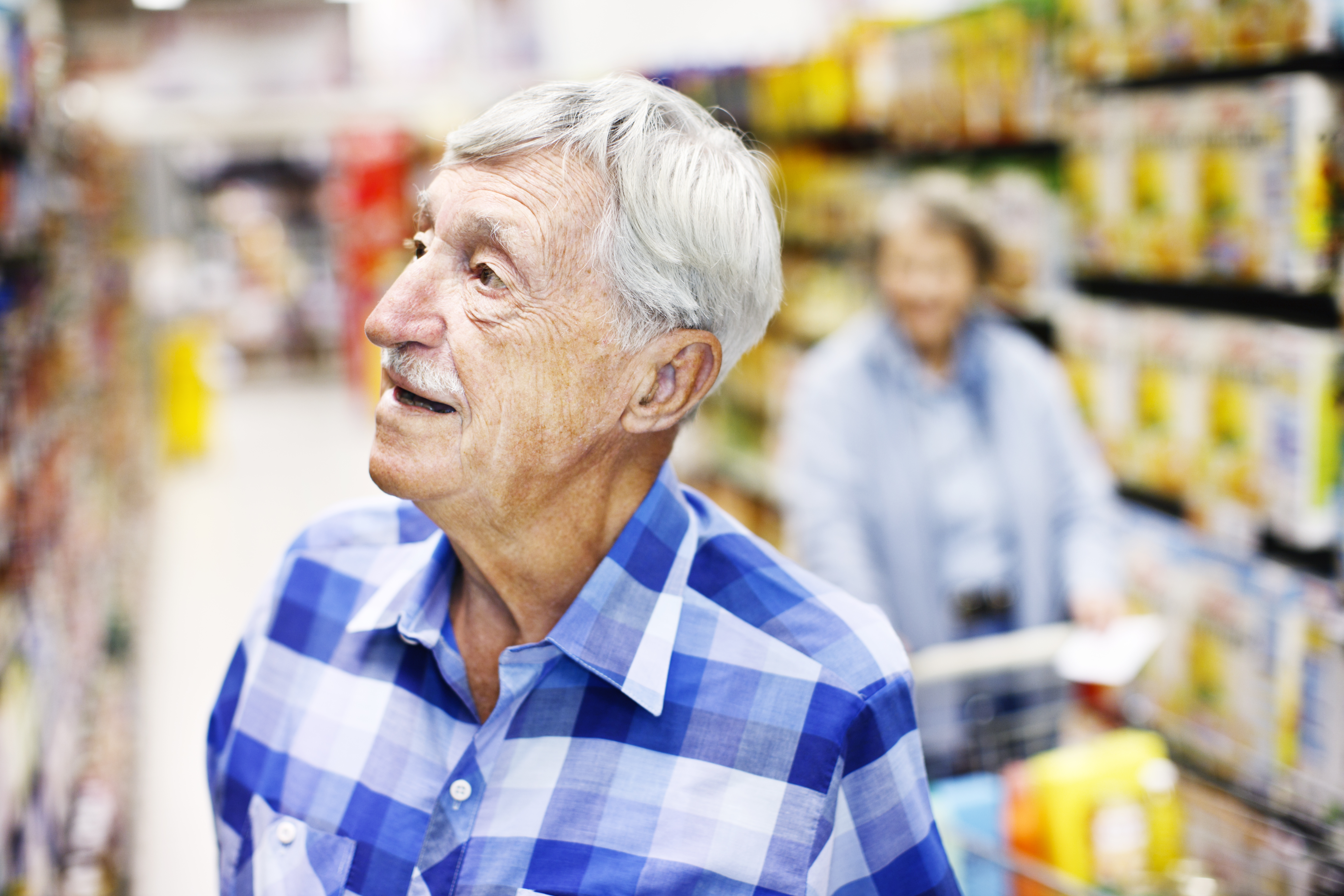 Serious senior man checks supermarket shelves seeking something