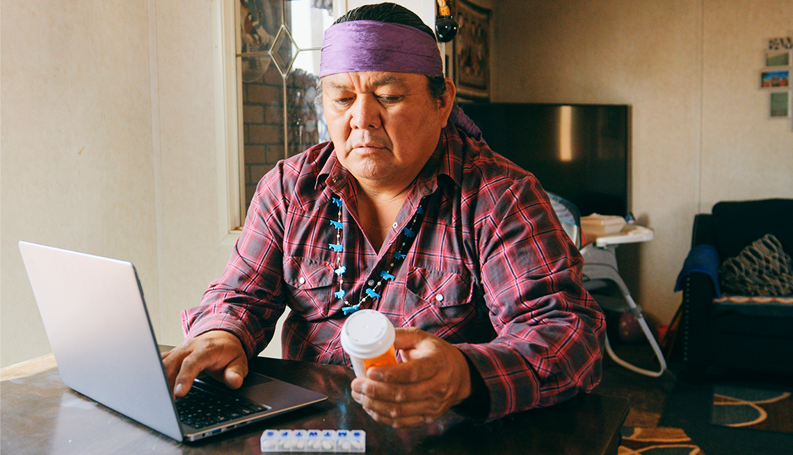 Older Native American man looks at laptop while holding prescription drug bottle.