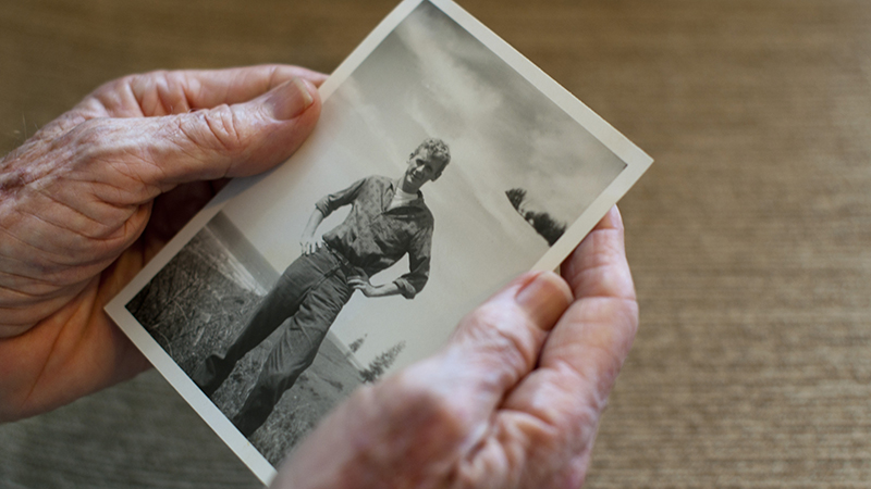 A close up of older hands holding an old photo of a young man