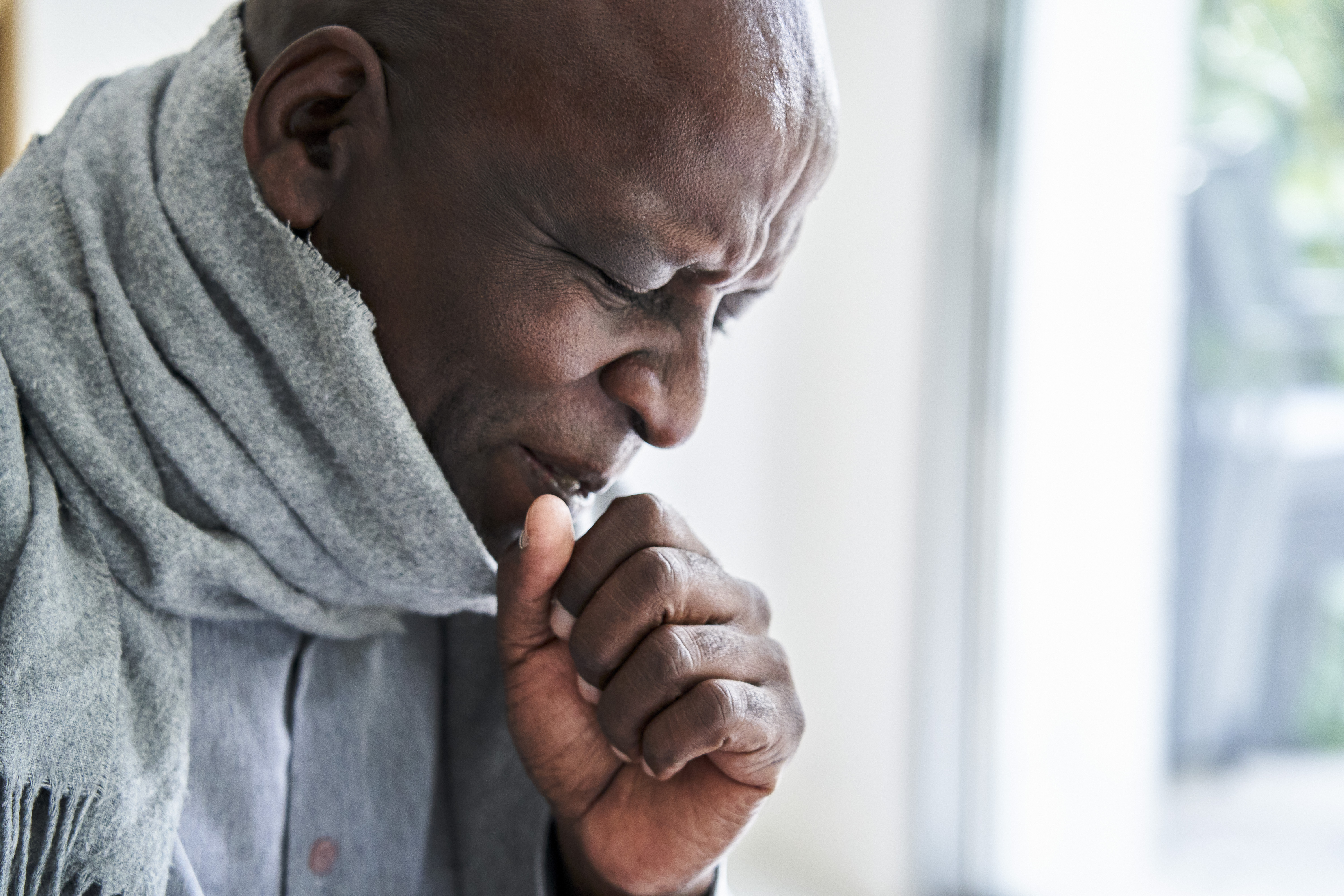Senior African-American man wearing a scarf and coughing in his hand