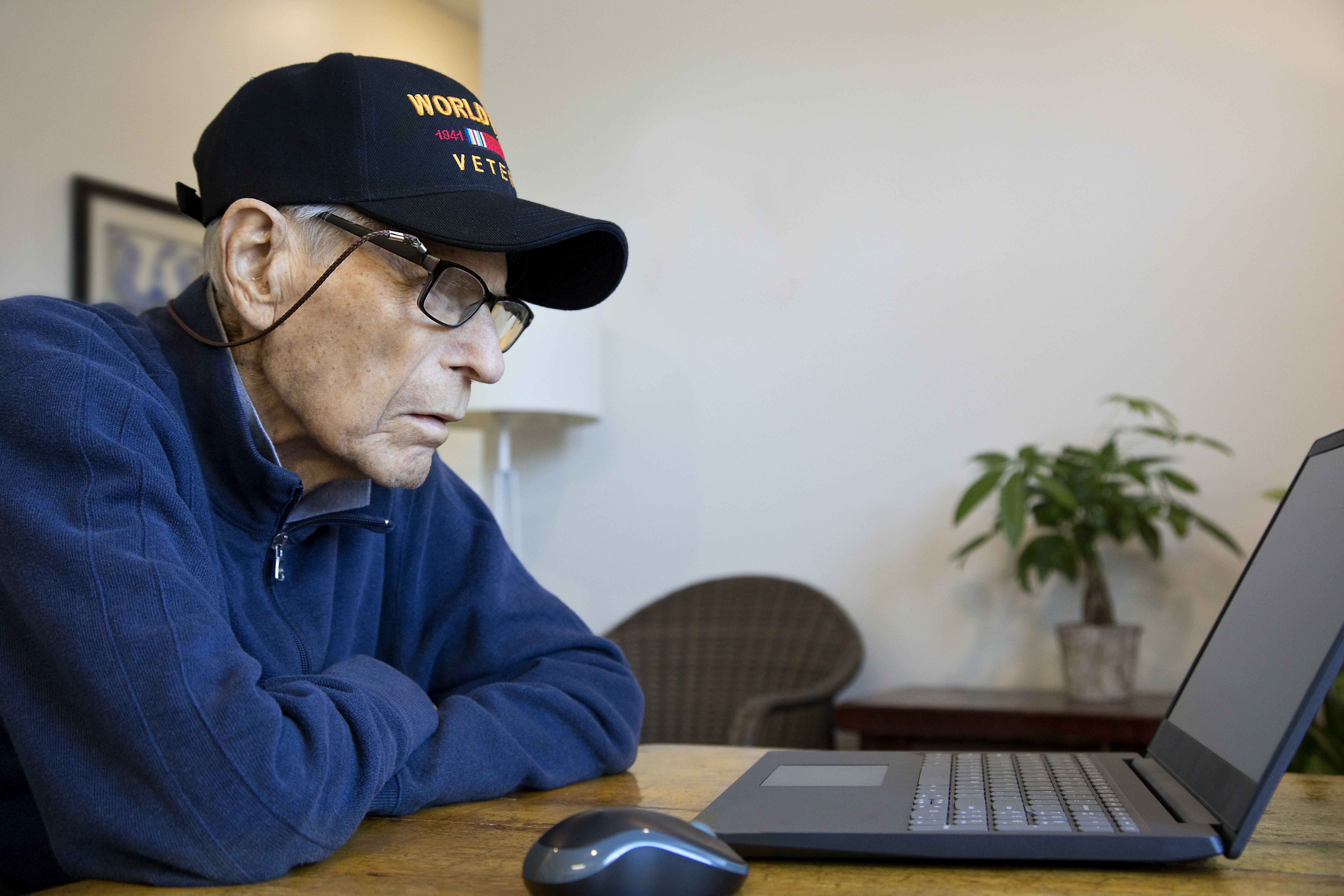 World War Two Veteran wearing cap at home looking at laptop