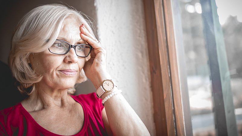 A woman with her hand on her head and looking out the window