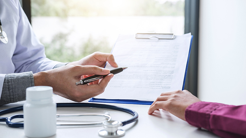 Hands complete paperwork on a clipboard in a medical setting.