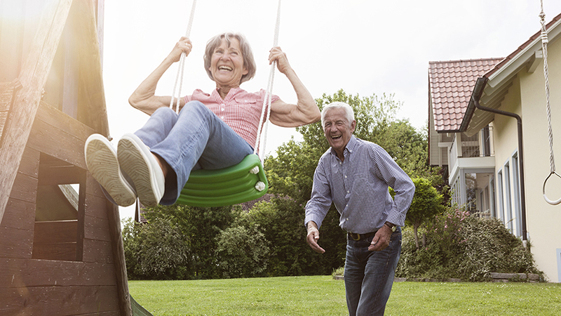 A woman on a swing being pushed from behind by a man