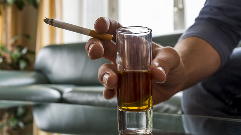 A close up of a hand holding a cigarette and shot glass