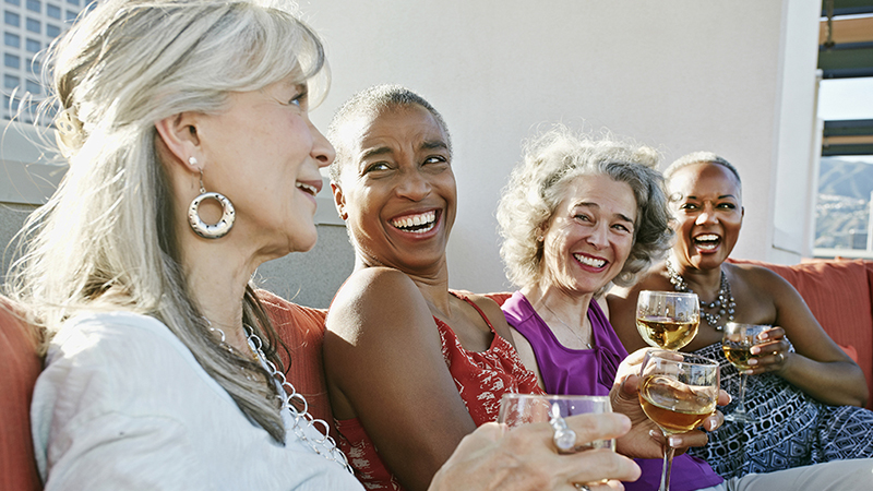 Four women drinking wine together on a couch on a rooftop