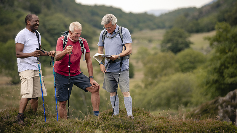 Three men hiking with hiking poles and looking at a map