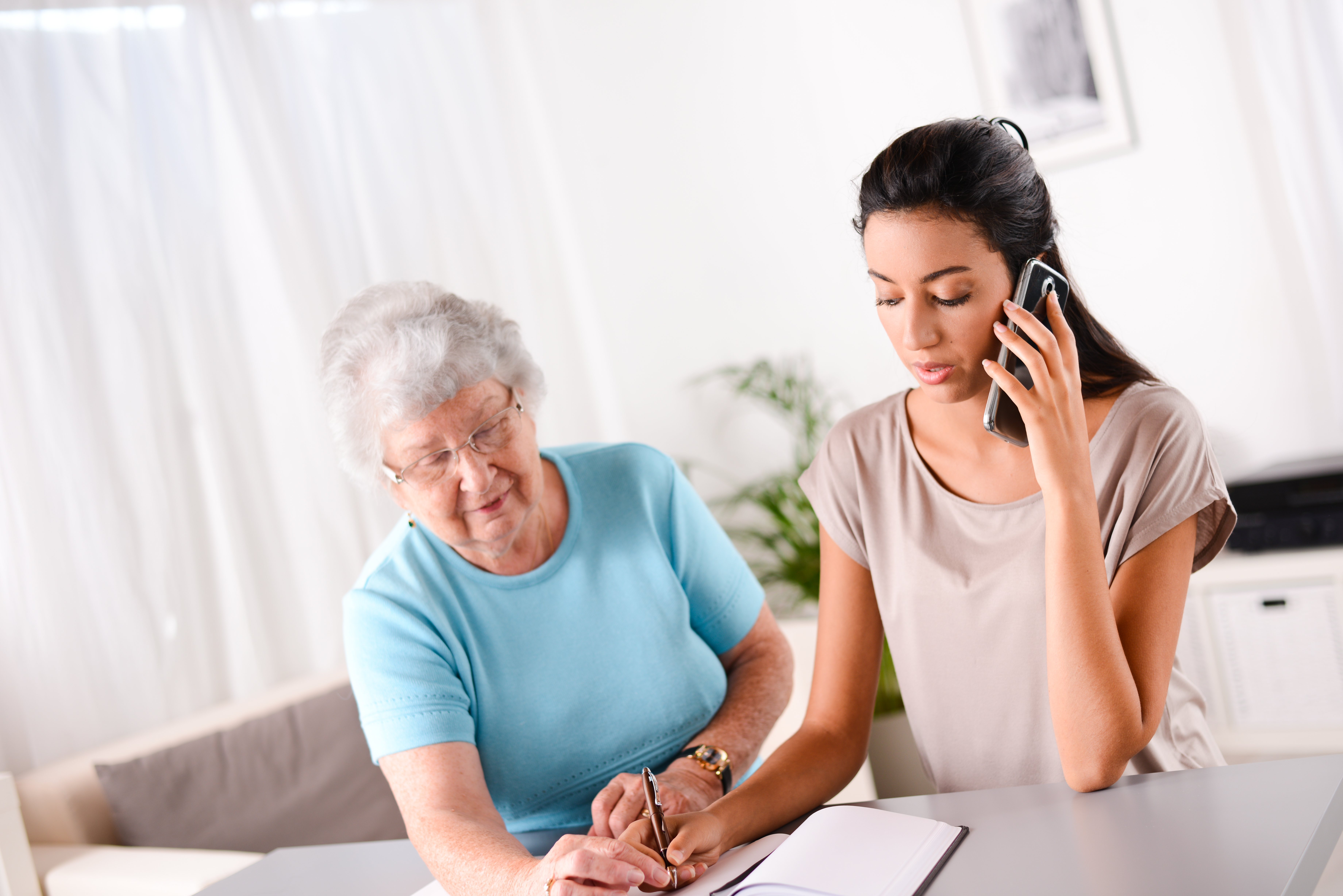 cheerful young woman helping old person paperwork and telephone call