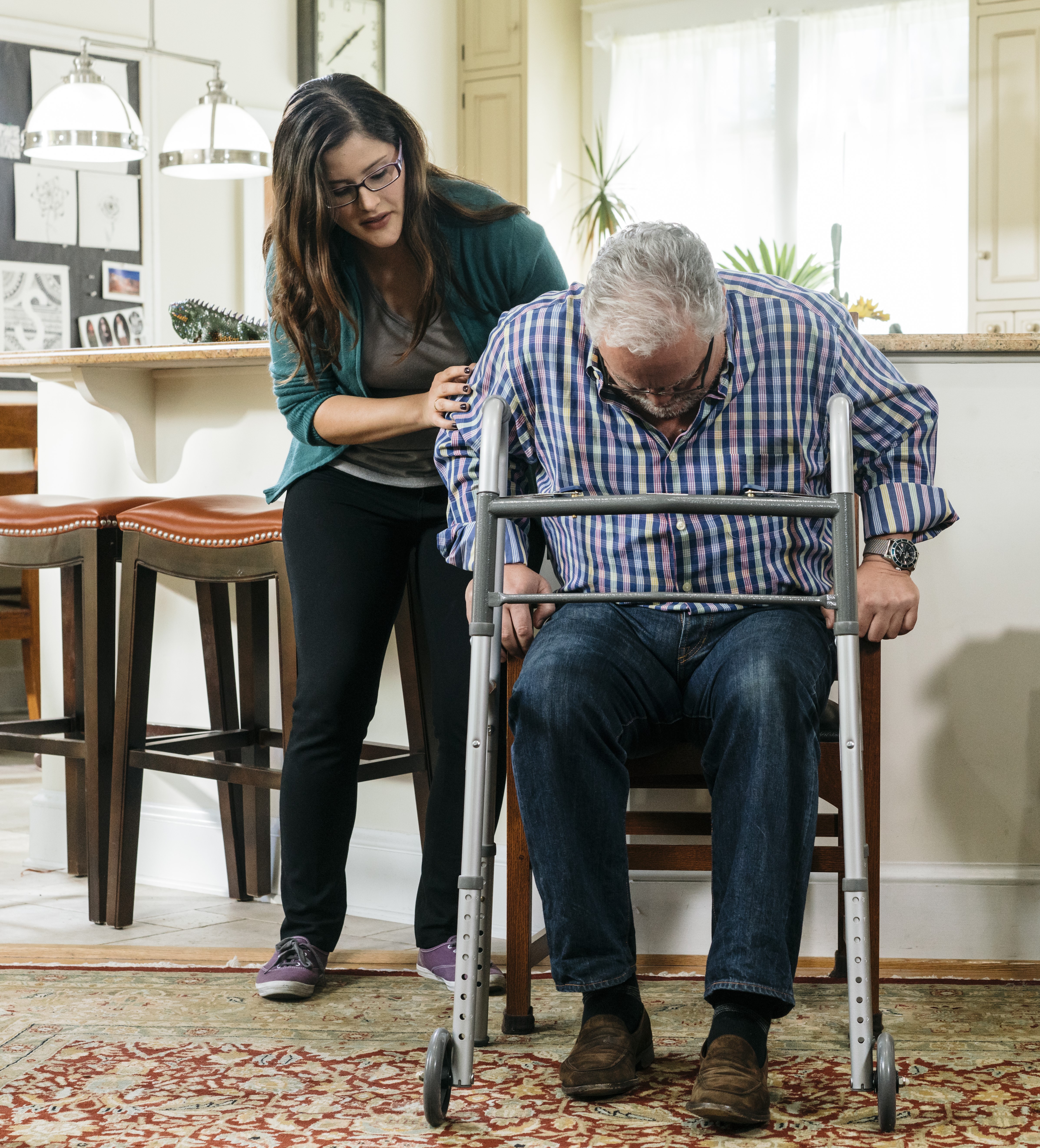 Young Hispanic woman helping her Hispanic father transfer from a seated to standing position using a walker as support.