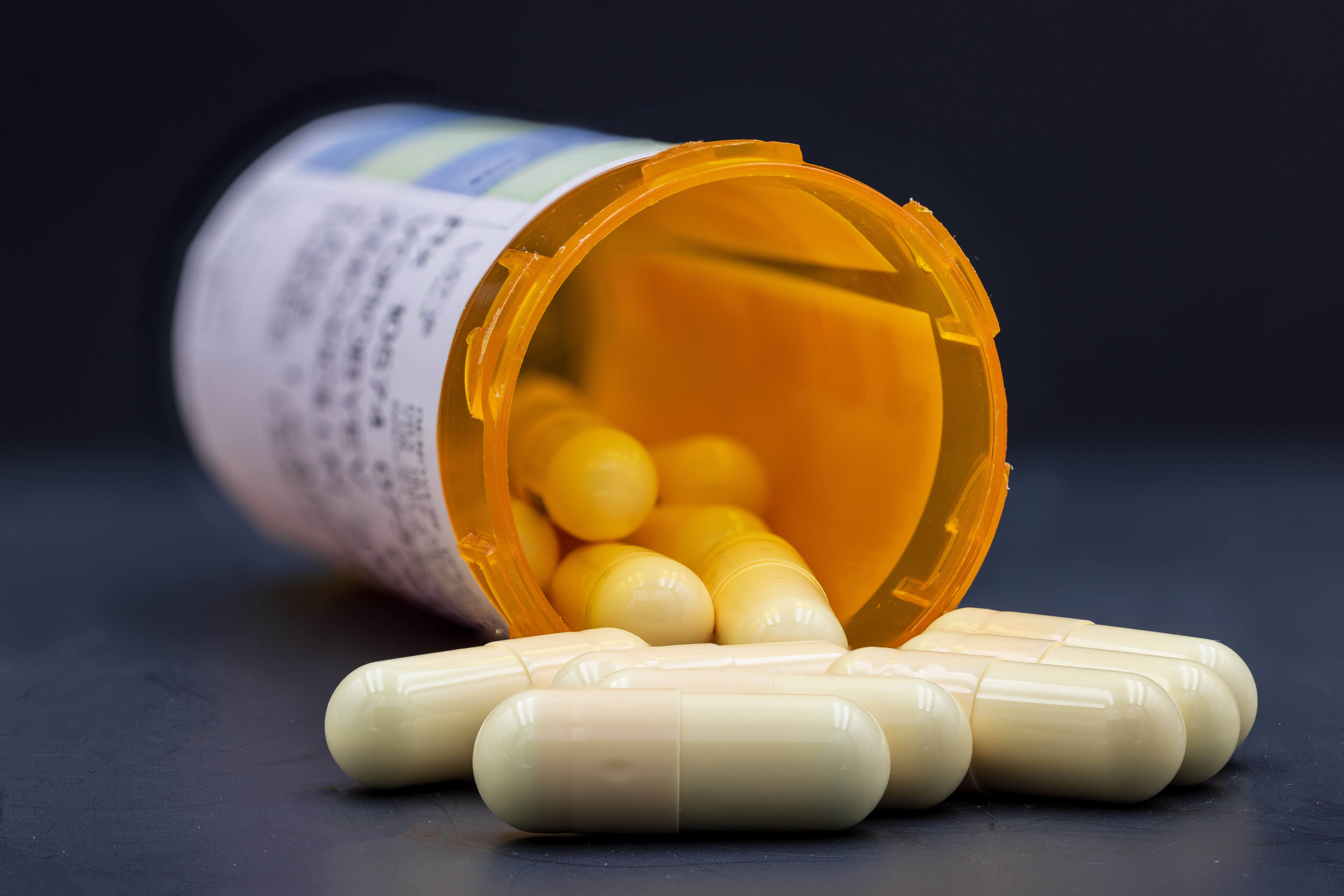 Closeup image of medical drugs spilling out of orange prescription bottle on black background