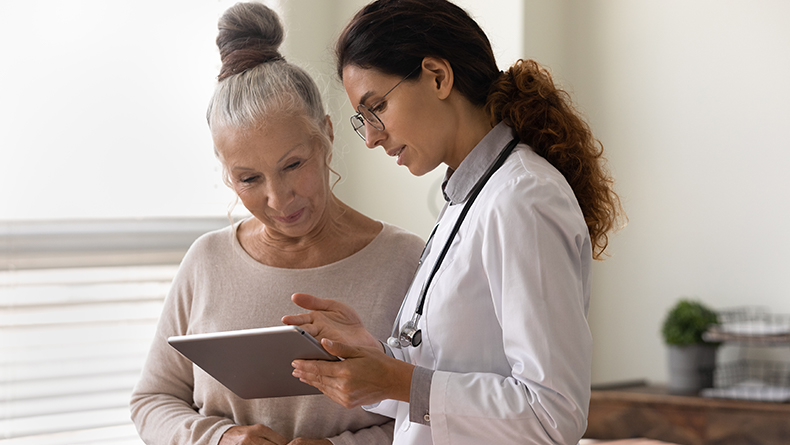 Serious GP doctor showing tablet screen to old 70s female patient, explaining electronic prescription, medical screening, examination result, giving consultation. 