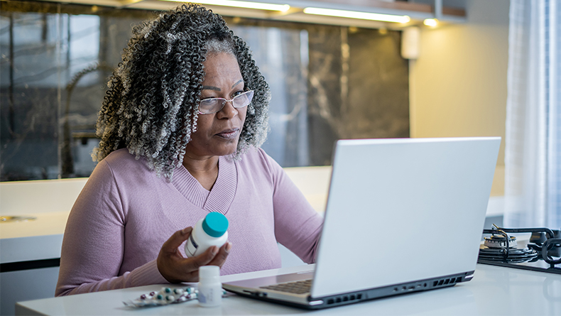 Senior woman on laptop for online doctor appointment and holding a prescription bottle.