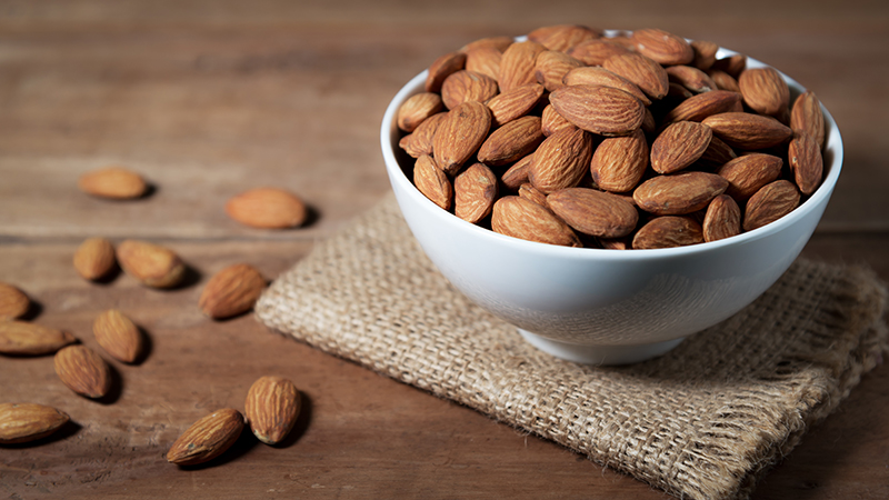 A close-up view of a bowl of almonds on a wooden table