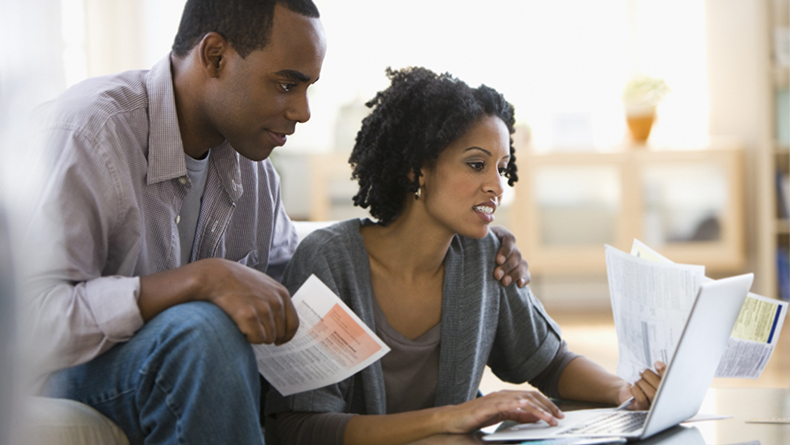 A Black couple sits together and looks at a computer screen while holding bills