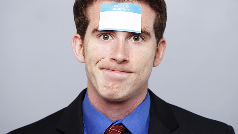 A man in a suit with a "My name is" sticker on his forehead