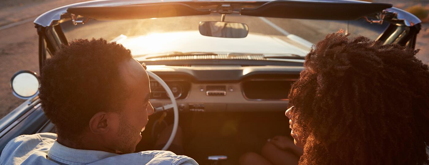husband and wife in convertible driving into the sunset talking to each other