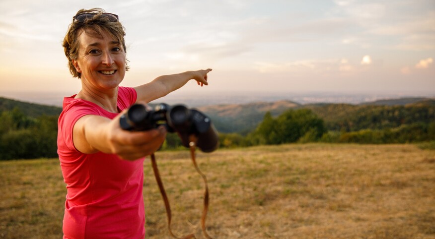 Woman giving you binoculars and pointing to where to look at in the distance