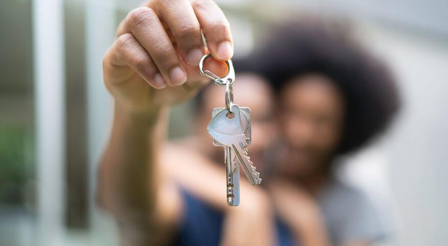 New homeowners holding keys in front of house with blurred background