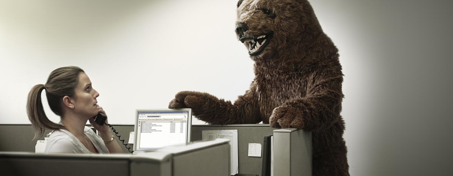 woman at work in cubicle with boss in bear costume standing over her desk