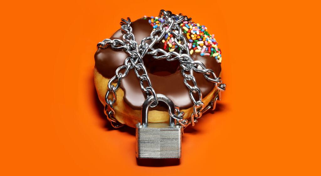 A chocolate frosted donut on an orange background with a chain and lock around it.