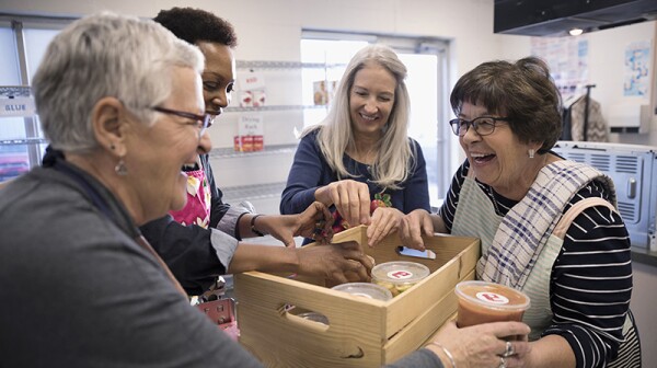 Female volunteers packing soup containers into crate in soup kitchen