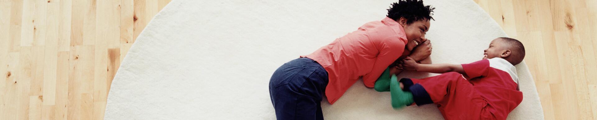 Mother and son (3-5) lying on rug, smiling, overhead view