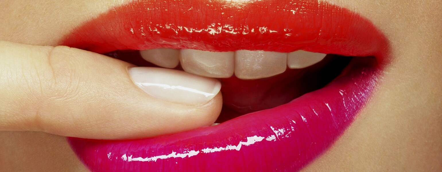 A close-up photo of a woman biting her finger in a flirty manner.