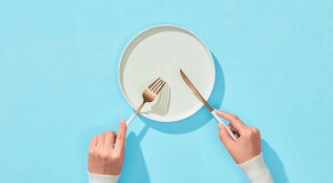 Hands with fork and knife and empty white plate on blue background 