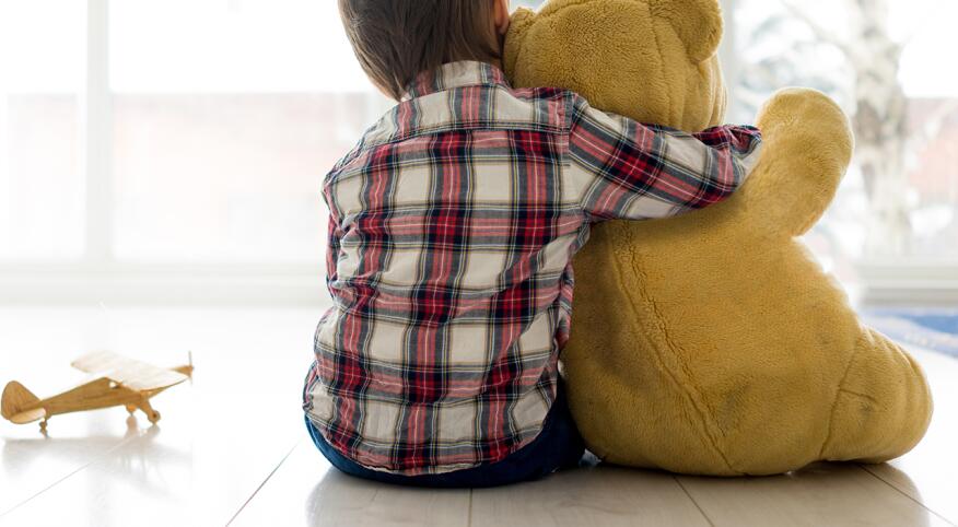 Rear view of child sitting in living room hugging Teddy bear