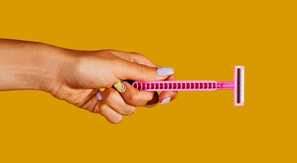 Woman's hand with colorful manicure holding a razor on yellow background