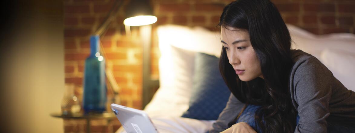 Woman lying on her bed looking at Google on her computer