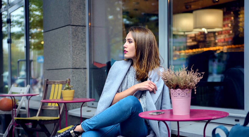 A woman in grey coat and blue jeans is waiting for someone at the cafe