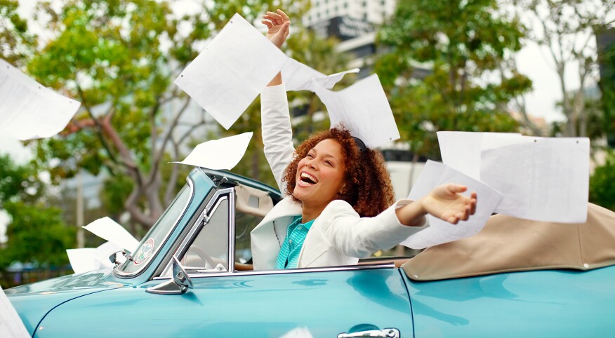 Happy woman in convertible throwing documents into the air