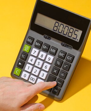 Hand typing numbers into calculator on yellow background