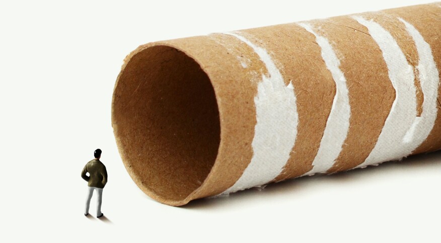 A small toy figure looking into an empty toilet paper roll