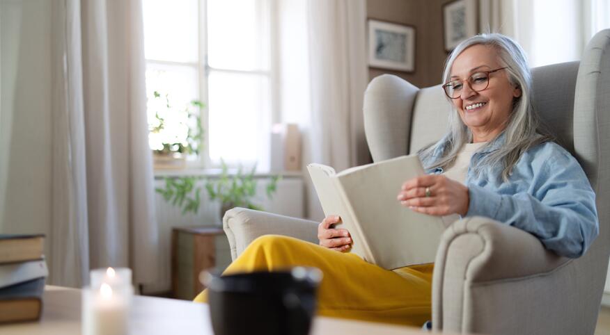 Happy senior woman sitting on sofa at home, reading a book.